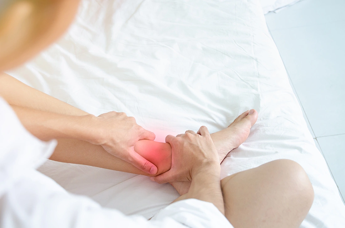 Woman holding her ankle while sitting on a sofa, representing chronic joint pain linked to ankle arthritis.