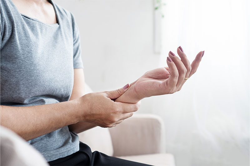 Woman clutching her wrist in pain and experiencing discomfort while sitting.