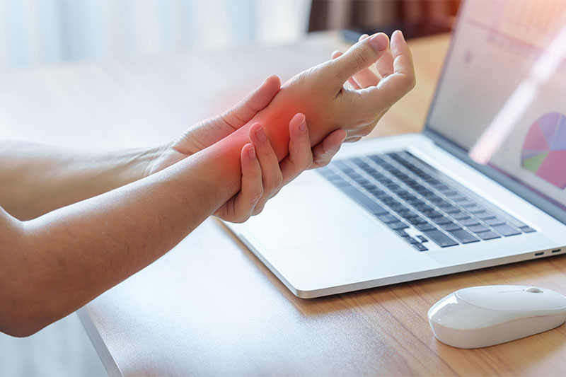Person holding their wrist in pain while working on a laptop.