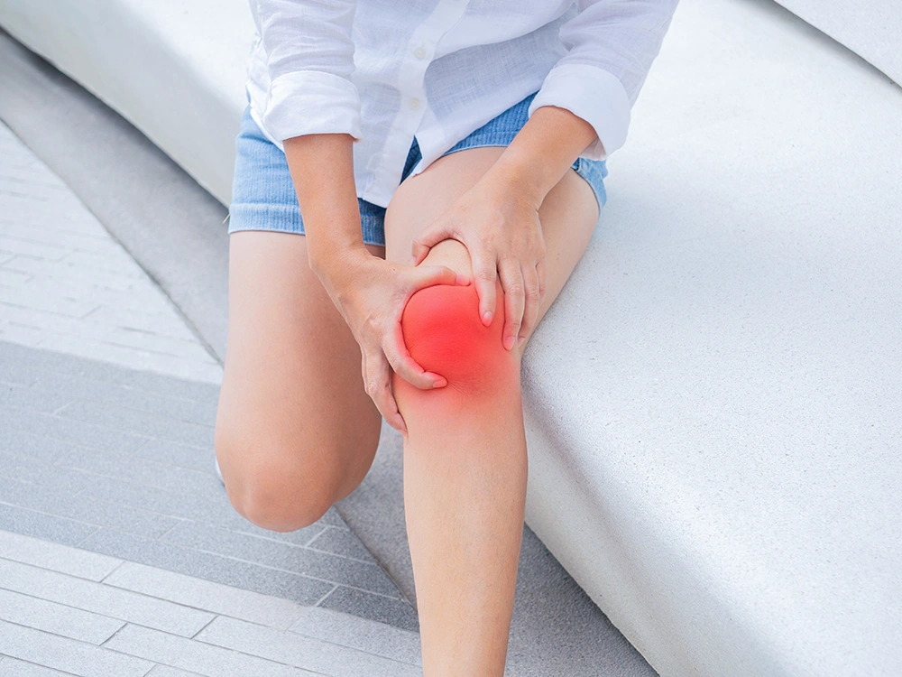 Woman seated while holding her knee and experiencing pain in the joint.
