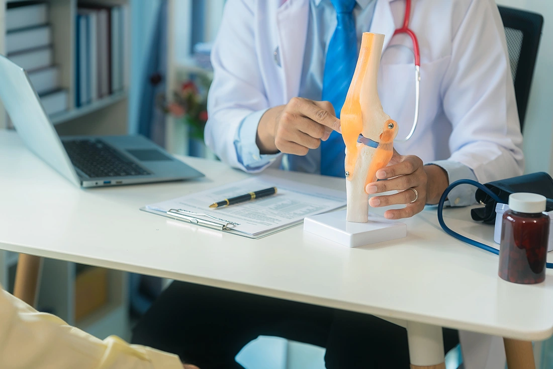 Orthopaedic specialist in clinical setting explaining knee anatomy to a patient during a professional consultation.