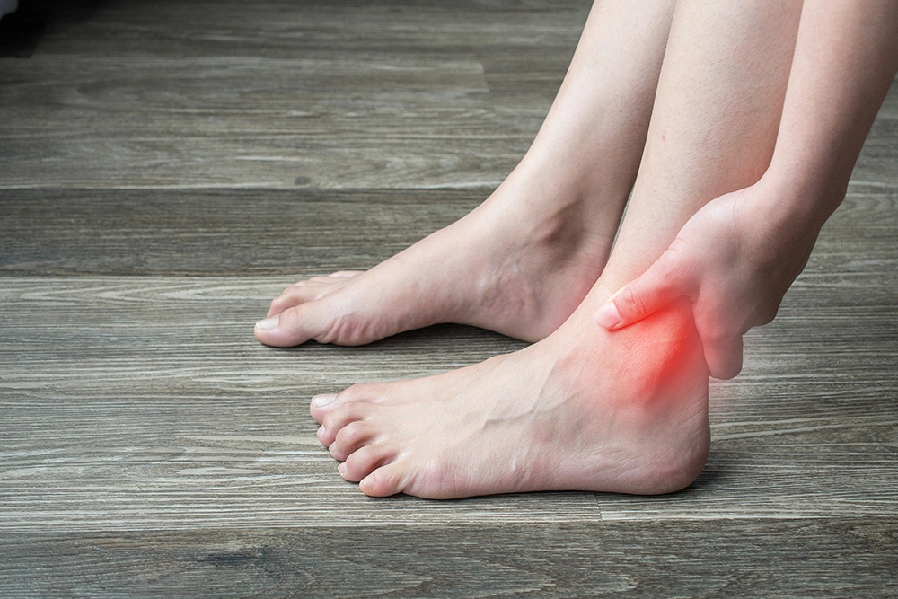 Close-up of a woman holding her ankle while experiencing foot and ankle pain.