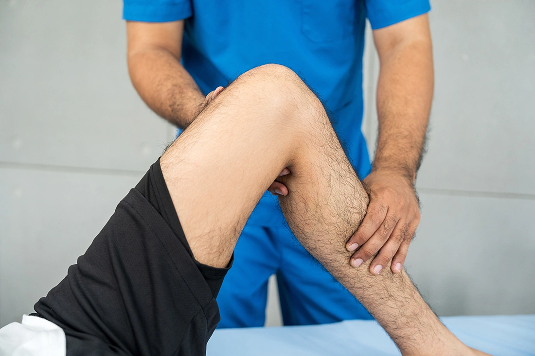 Healthcare professional assisting an athlete with leg support during sports injury treatment in a clinical setting.