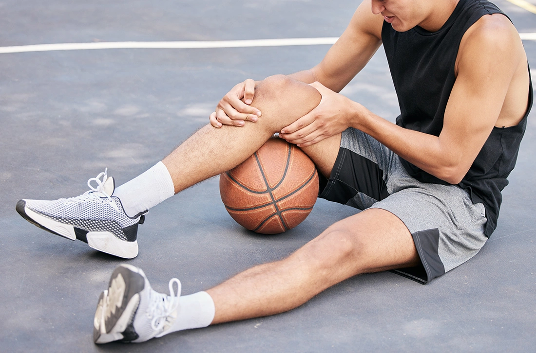 Basketball player clutching his knee on court after sports injury.