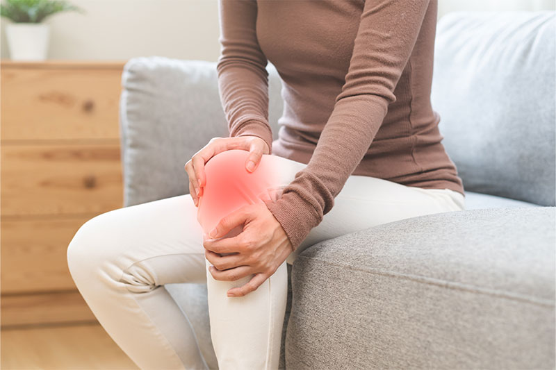 A woman clutching her knee, illustrating knee pain and joint inflammation.