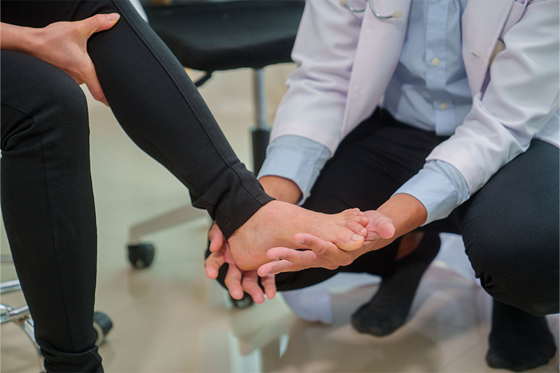 Doctor examining a woman’s injured ankle during a clinical consultation.