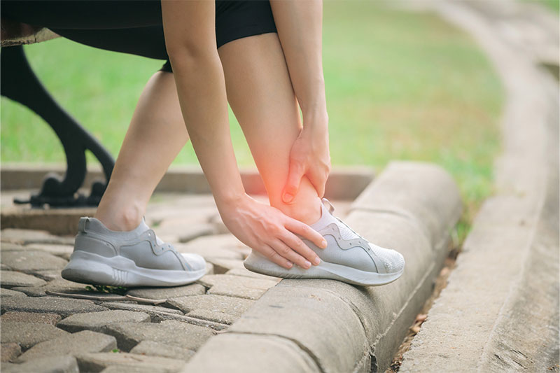 Female jogger holding her ankle in pain, suggesting a possible sprain.
