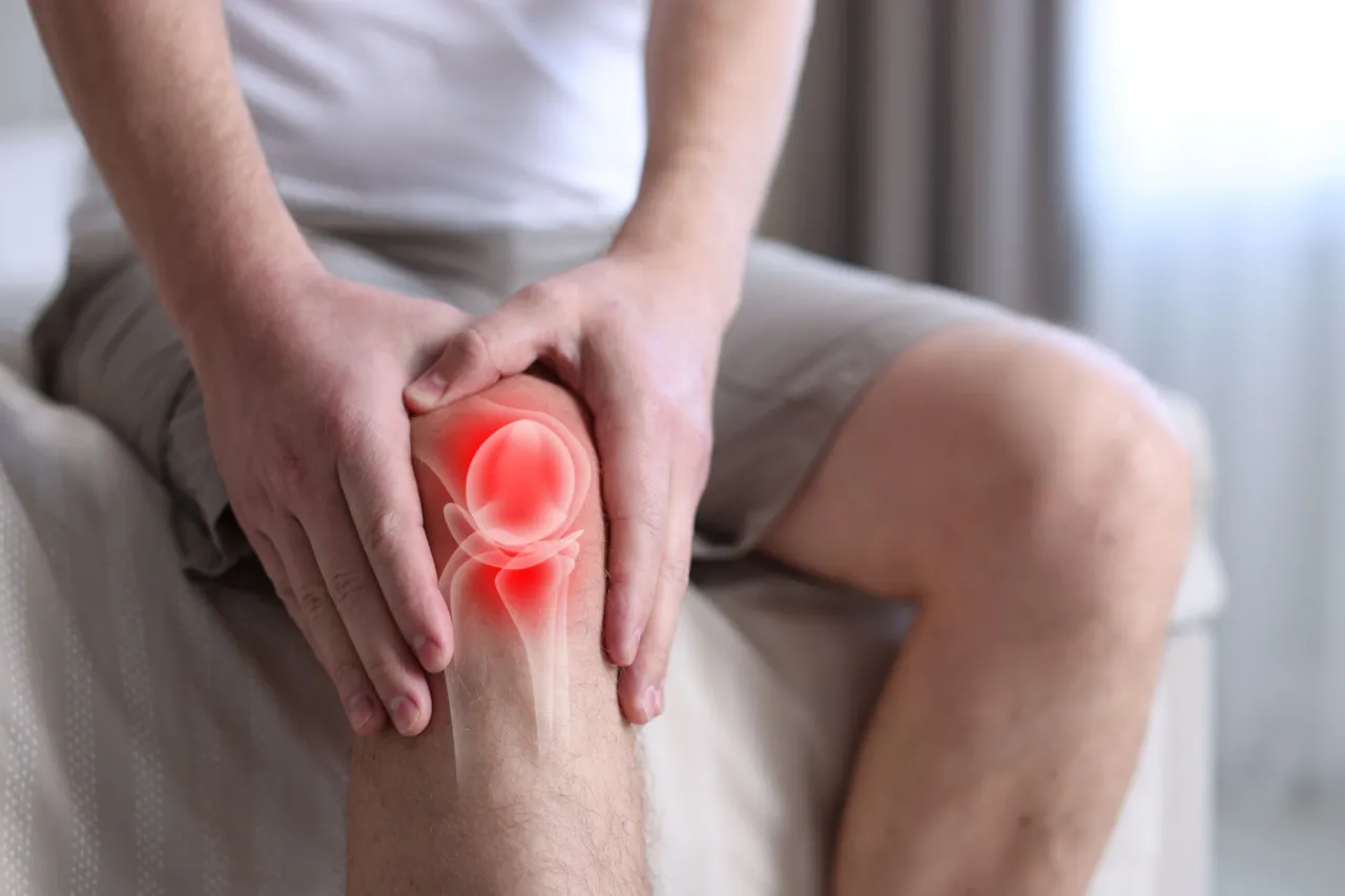 A man holding a painful knee with an anatomical overlay highlighting joint inflammation and knee pain treatment